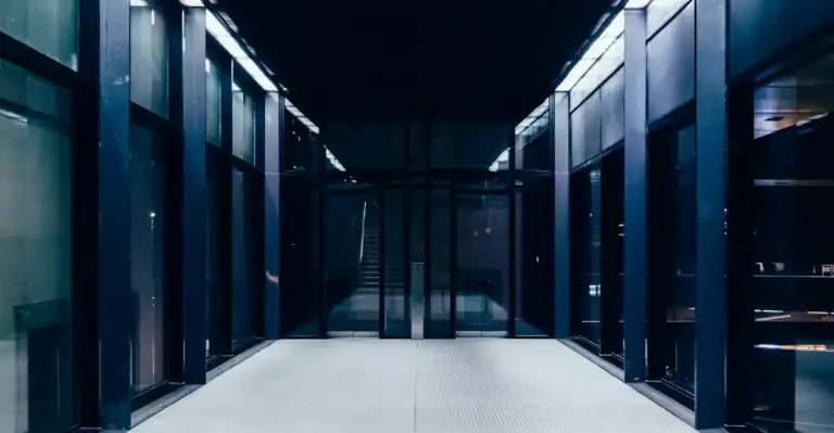 Couloir sombre aux parois vitrées éclairé par des néons, illustration du comparatif AWS vs Azure vs Google Cloud