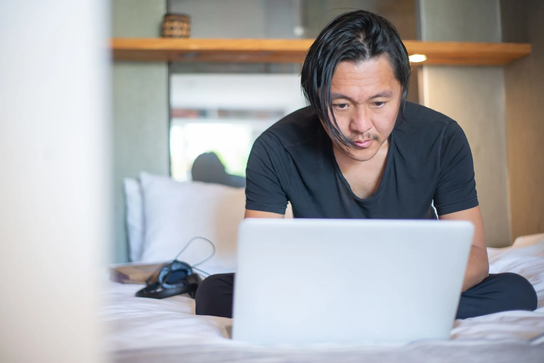 An Asian man working from home on a laptop, focusing on his digital tasks in a cozy indoor setting.