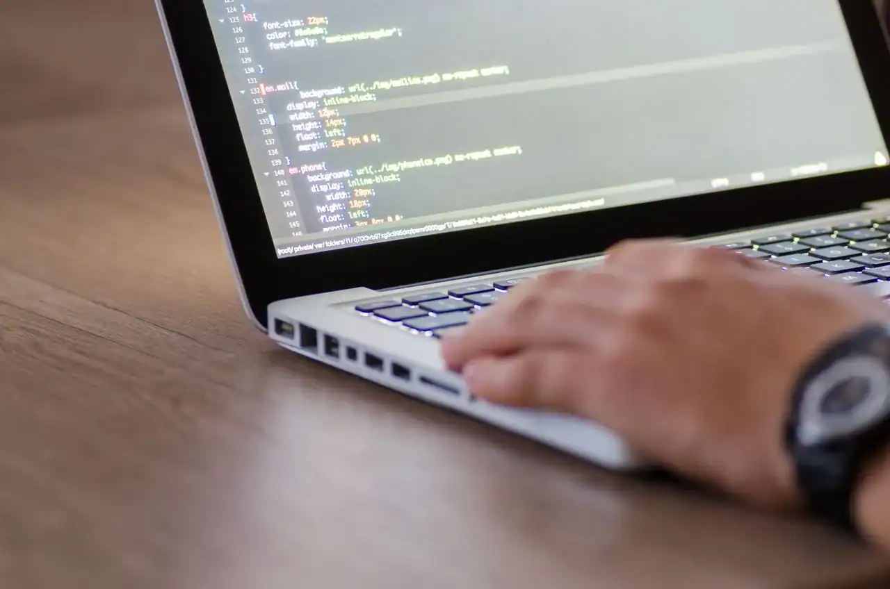 Développeur tapant du code sur un ordinateur portable posé sur un bureau en bois