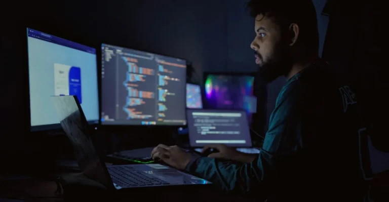 Développeur de profil devant plusieurs écrans affichant du code dans une pièce sombre