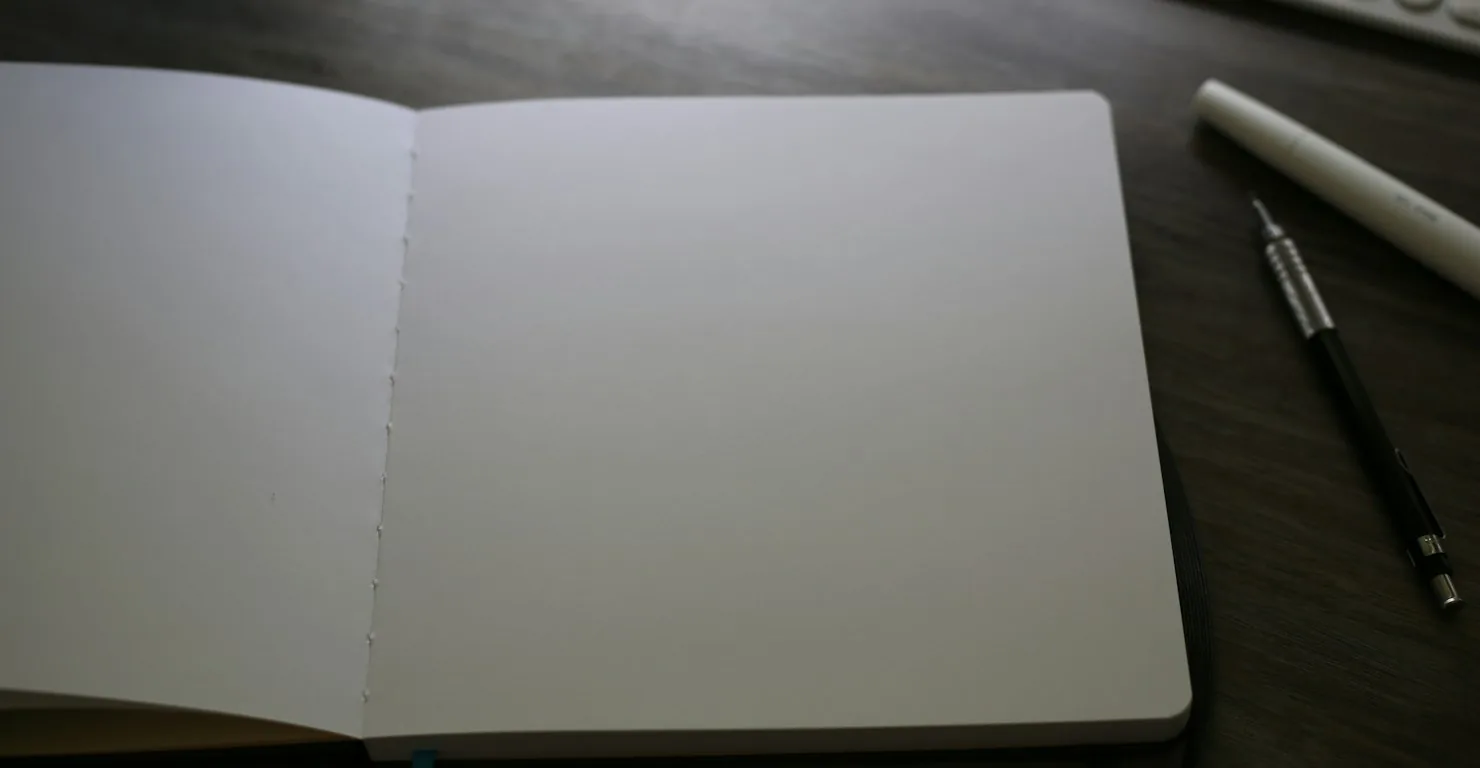 Carnet ouvert aux pages blanches posé sur un bureau sombre à côté d'un porte-mine, illustration d'un portfolio développeur à construire